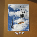 Ski Lift and Sky Jigsaw Puzzle<br><div class="desc">Two empty ski lift chairs hang from their lift cables in this striking photograph. With no riders, the ski lift looks like a black linear diagram in front of an expansive view of blue sky and white puffy clouds. The upper right chair heads uphill and the lower left chair returns...</div>