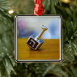 SlipperyJoe's Hanukkah traditional toy gifts close Metal Ornament<br><div class="desc">SlipperyJoe's Hanukkah traditional toy gifts close-up metallic dreidel resting visible etched Hebrew letter Shin ש Nes Gadol Haya Sham great miracle happened there artistic festive blurred Bokeh background tradition storytelling small rituals themes warm organic grain wooden surface backdrop glows soft colorful lights four-sided silver metal spinning top reds greens yellows...</div>