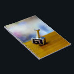 SlipperyJoe's Hanukkah traditional toy gifts close Notebook<br><div class="desc">SlipperyJoe's Hanukkah traditional toy gifts close-up metallic dreidel resting visible etched Hebrew letter Shin ש Nes Gadol Haya Sham great miracle happened there artistic festive blurred Bokeh background tradition storytelling small rituals themes warm organic grain wooden surface backdrop glows soft colorful lights four-sided silver metal spinning top reds greens yellows...</div>