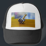 SlipperyJoe's Hanukkah traditional toy gifts close Trucker Hat<br><div class="desc">SlipperyJoe's Hanukkah traditional toy gifts close-up metallic dreidel resting visible etched Hebrew letter Shin ש Nes Gadol Haya Sham great miracle happened there artistic festive blurred Bokeh background tradition storytelling small rituals themes warm organic grain wooden surface backdrop glows soft colorful lights four-sided silver metal spinning top reds greens yellows...</div>