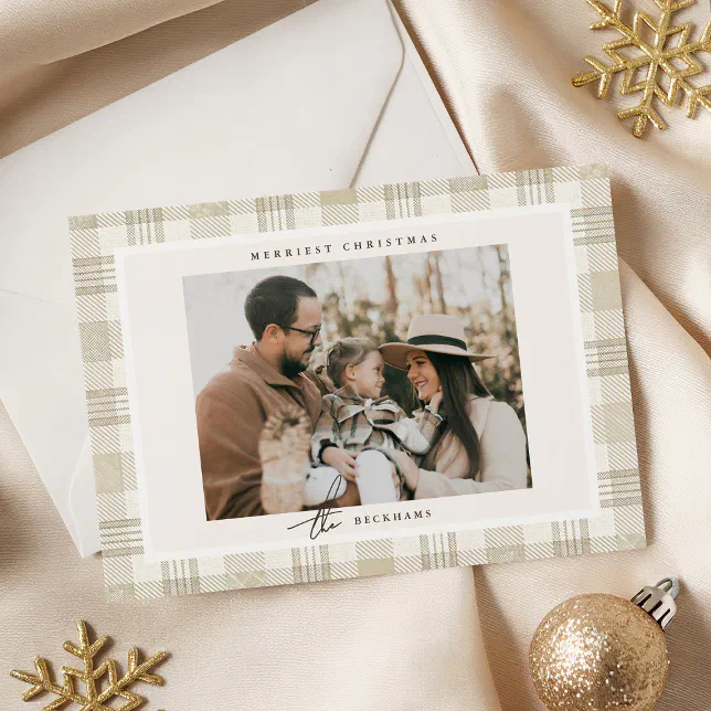 A beige plaid holiday card is shown in front of a white envelope on a cream background with some gold tree and tree ornaments.