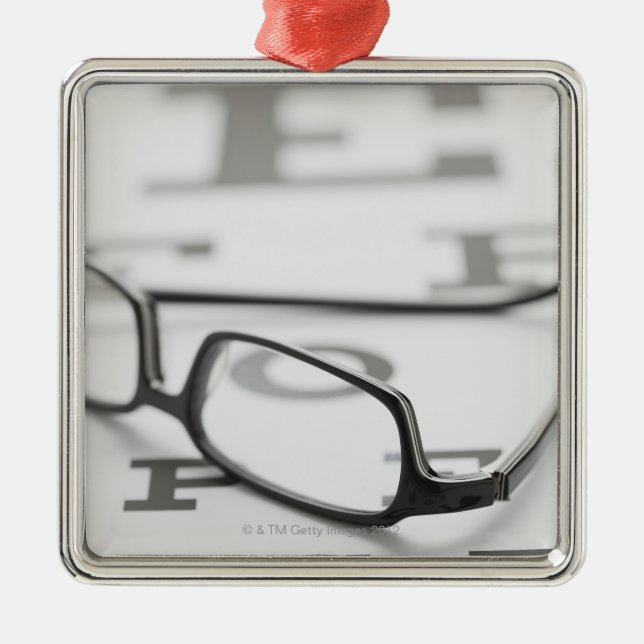 Studio shot of eyeglasses on eye chart metal ornament (Front)