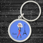 Stylish White Hair Girl Red Pants by Eiffel Tower  Keychain<br><div class="desc">The illustration on this keychain depicts a stylish, white hair girl carrying a white bag, walking by the Eiffel Tower in Paris on a blue background. She's wearing red pants, a grey jacket, grey gloves and grey boots. Her name, Emma, is written beside her in an elegant black font that...</div>