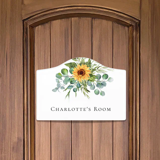A dorm room door sign that says "Charlotte's Room" with a sunflower design, placed on a dark brown wooden door.