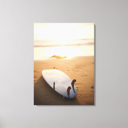 Surfboard laying on beach at sunset canvas print