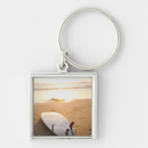 Surfboard laying on beach at sunset keychain