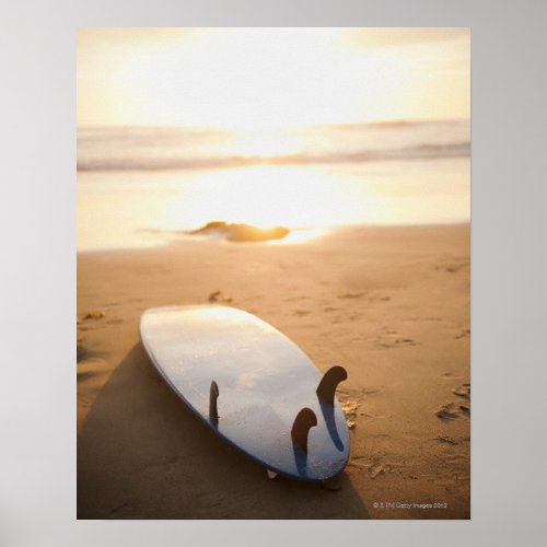 Surfboard laying on beach at sunset poster