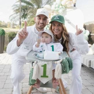 A family dressed in golf attire sits outdoors with a baby in a high chair, surrounded by golf-themed decorations in green and white. The scene feels bright, playful, and styled like a first birthday celebration.