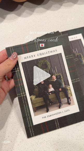 A plaid-bordered holiday photo card with a family portrait, held against a marble countertop. Warm, festive, family-keepsake mood.