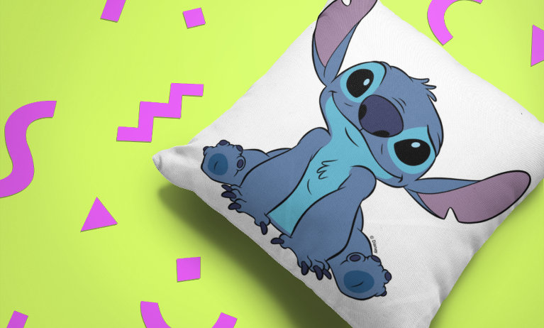 White throw pillow featuring a large graphic of Stitch reaching toward the camera, set against a lime green background decorated with pink geometric shapes.