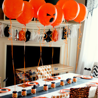 A cheerful orange-and-black Halloween room decorated with jack-o’-lantern balloons, spooky garlands, and themed tableware. The mood is playful, festive, and family-friendly.