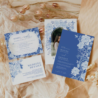 A blue and white baby shower invitation suite with floral patterns and elegant typography arranged on soft fabric. The design feels classic and delicate with a traditional, refined style.