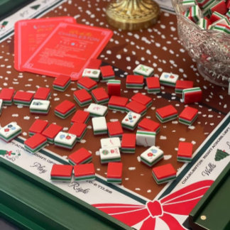 Looking at the two images:  Festive mahjong set on a green table, red and green tiles scattered across a holiday mat with a painted red bow. Coral reference cards and a cut-glass bowl sit nearby. Warm, cozy, celebratory mood with a classic Christmas palette.