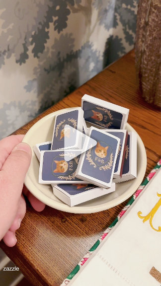 Pet-illustrated matchboxes in navy and gold, piled in a bowl against floral wallpaper. Charming, whimsical, holiday-hosting mood.