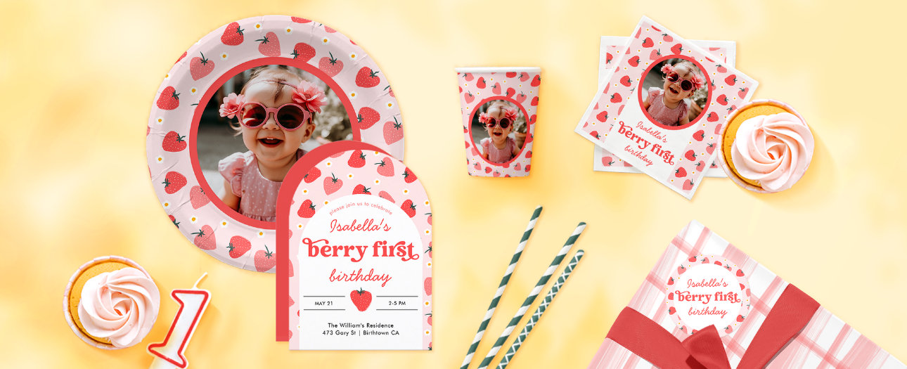 The image showcases a delightful "Berry First" birthday celebration with a charming strawberry theme. A pink and red color palette runs throughout, with playful strawberry patterns adorning the plates, cups, napkins, and invitations. A custom photo plate and napkins feature the birthday child’s smiling face, bringing a personal touch to the setup. Sweet details like soft pink cupcakes, a number one candle, striped paper straws, and a gingham-wrapped gift complete the festive scene, all set against a warm yellow background that enhances the cheerful atmosphere.