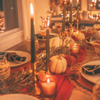 A warmly lit tablescape with pumpkins, candles, and wine glasses styled for an intimate dinner. The palette is cozy and autumnal, perfect for gathering in gratitude.