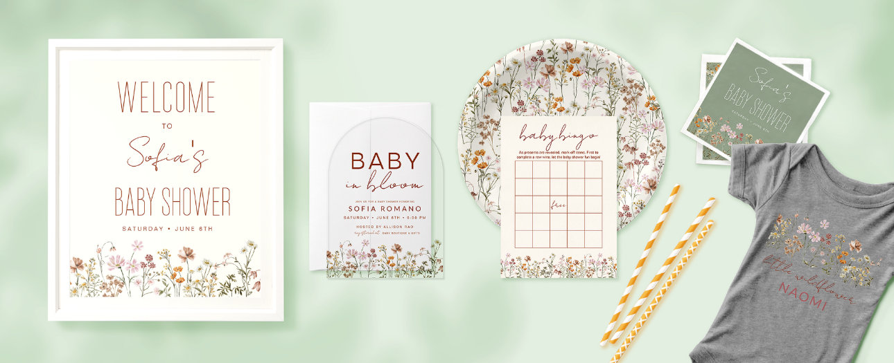 The image showcases a "Baby in Bloom" baby shower theme with a soft botanical aesthetic. A framed welcome sign with elegant typography and a floral border sets the tone. The arched acrylic invitation features warm lettering and matching floral accents. A round paper plate with a wildflower pattern complements a baby bingo card with a grid and instructions. Green napkins display "Sofia’s Baby Shower" in white script with floral details. A gray baby onesie reads "little wildflower Naomi" alongside a floral illustration. Yellow and white patterned paper straws complete the cohesive setup, all set against a pastel green background.