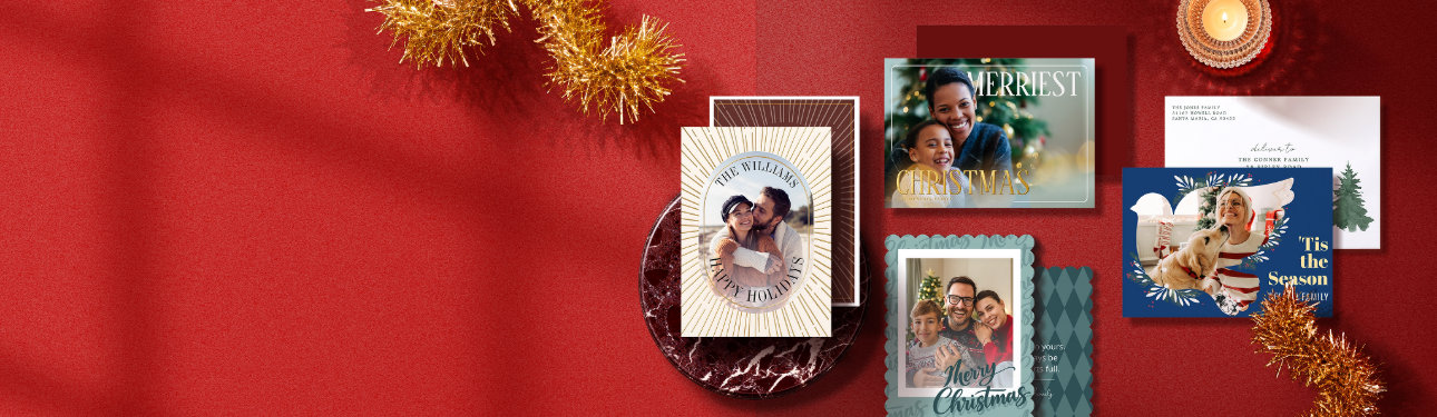Personalized Christmas photo cards in gold, green, and navy designs arranged on a festive red background with tinsel and candlelight.