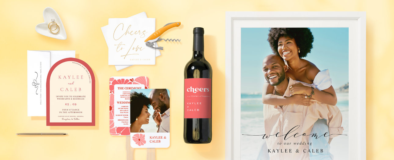 The image showcases a stylish wedding celebration with a warm, modern aesthetic. A personalized invitation, wine bottle, and welcome sign feature elegant typography in a red and cream color scheme. Thoughtful details like engraved napkins, a custom ceremony fan, and a corkscrew add a refined touch. A joyful couple's framed photo completes the setup, set against a soft yellow background.
