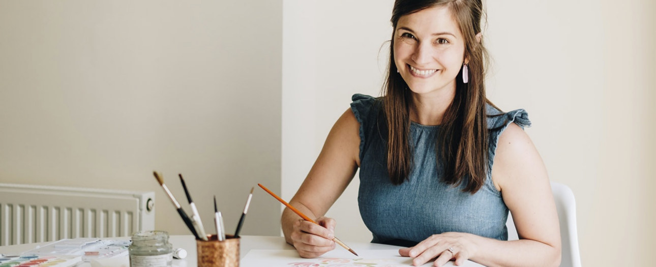 An image of creator Annie Montgomery smiling into the camera as she paints.