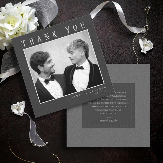 A black-toned wedding thank you card. Two men in suits are pictured looking at each other. Both sides of the card can be seen, and a white flower and ribbon are in the background.