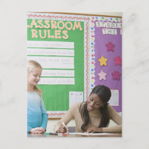 Teacher grading girls paper in classroom postcard