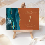 Teal Gold Agate Burnt Orange Wedding Table Number<br><div class="desc">The left-hand edge of this elegant modern wedding table number card features a teal blue watercolor agate border trimmed with faux gold glitter. The customizable text combines gold-colored handwriting,  italic and copperplate fonts on a burnt orange background.</div>