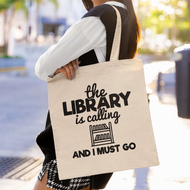 The Library Is Calling And I Must Go Reading Books Tote Bag (This tote bag is perfect for book lovers who can’t resist the call of the library.)