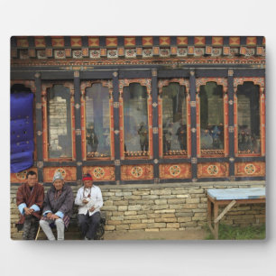 Three men sit on a bench at the Memorial Chorten Plaque