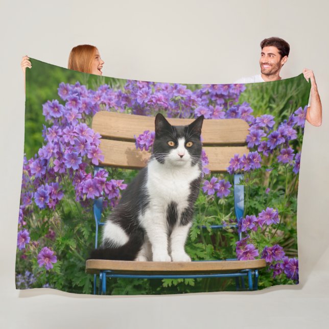 Tuxedo cat sitting on a garden chair with flowers fleece blanket (In Situ)