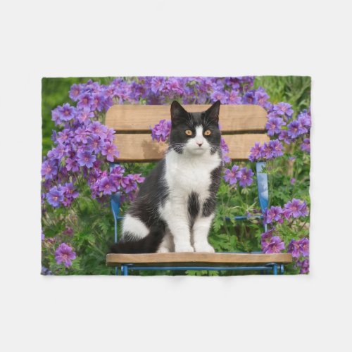Tuxedo cat sitting on a garden chair with flowers fleece blanket