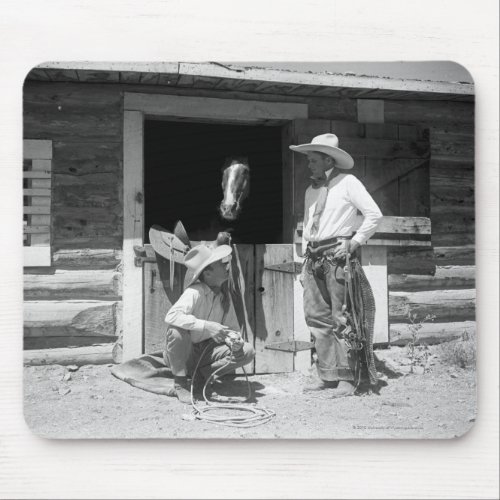 Two cowboys standing next to a barn with a horse mouse pad