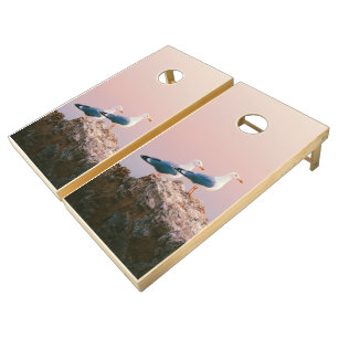 Two seagulls sitting on a rock in front of a pink cornhole set