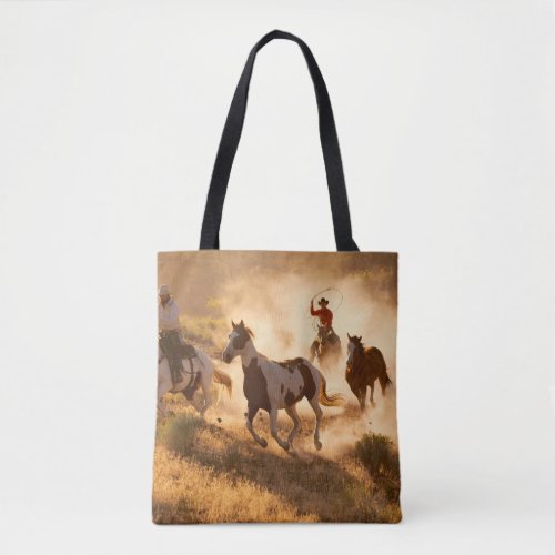 Two western cowboys riding horses roping wild hor tote bag