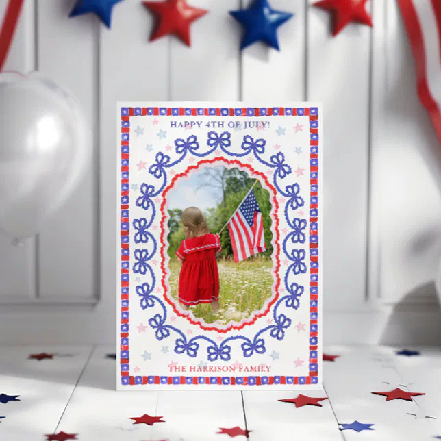A 4th of July card with a child holding the American flag on the front of it. Red, white, and blue décor can be seen hanging behind it.