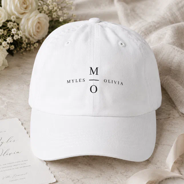 A simple white monogram baseball hat. In the background there is a white rose bouqet and a card. 



