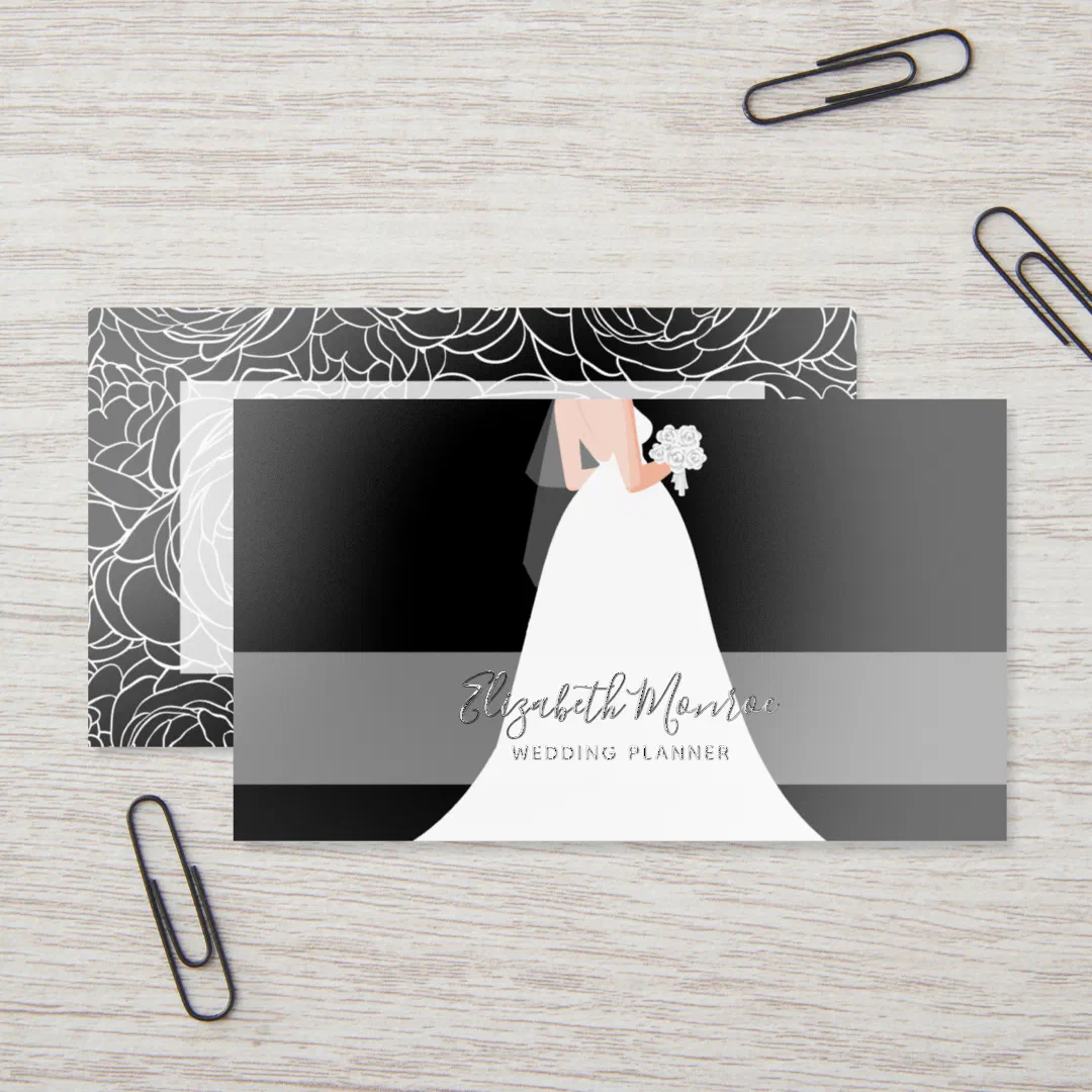A black, white and gray business card with a bride on the front and a floral abstract design on the back. It's placed on a wooden table with black paper clips scattered.