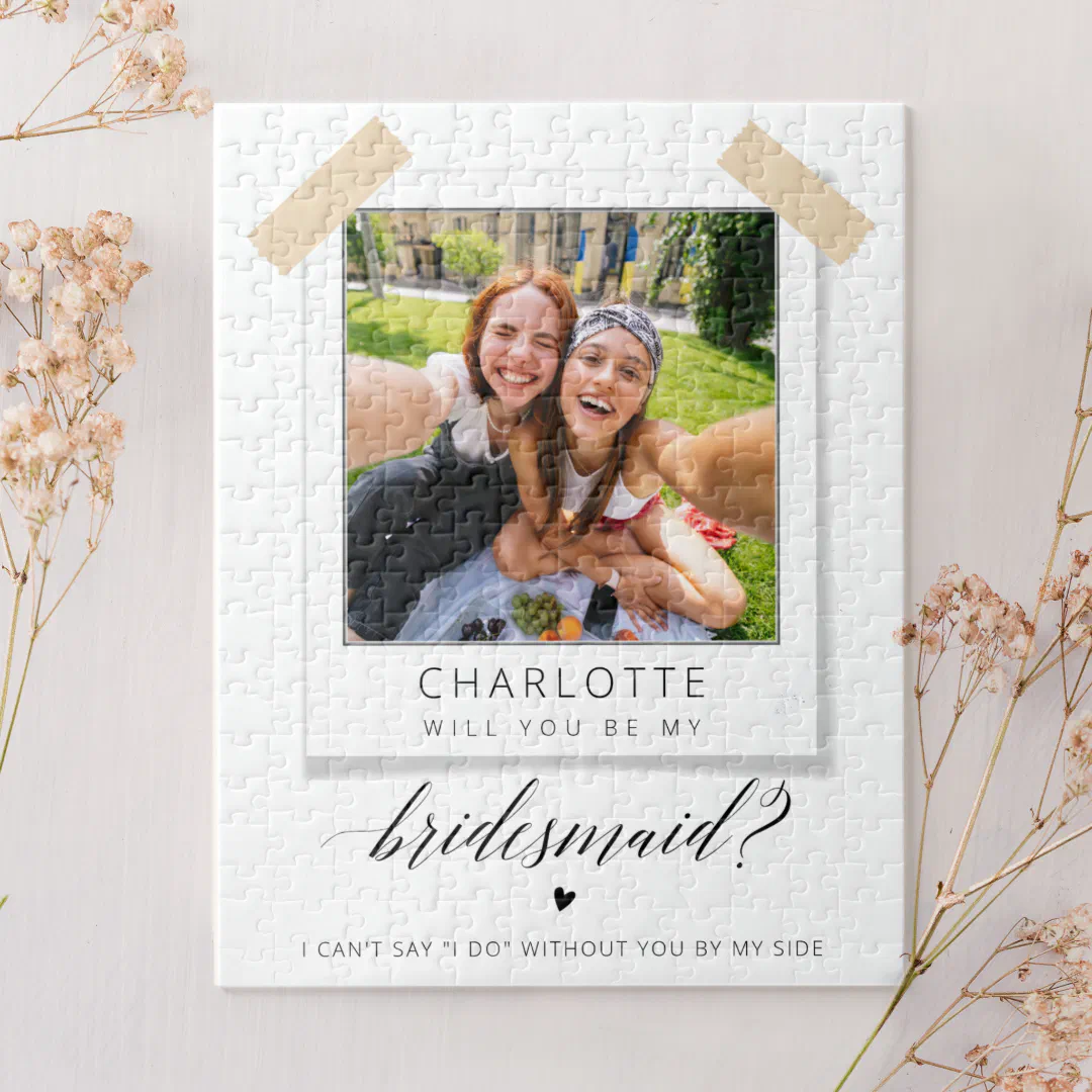 Jigsaw puzzle with a polaroid photo of the bride and bridesmaid in the center. Black scripted text and little black heart that's centered. In the background you'll find a few pink flower sprigs and a back colored to match.