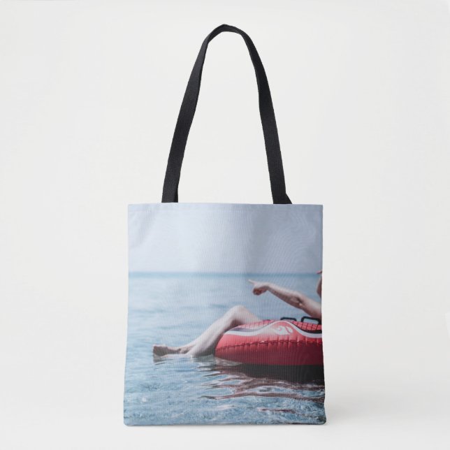 Woman on an inflatable float in the ocean pointing tote bag (Front)