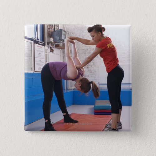 Woman stretching with trainer in gym pinback button