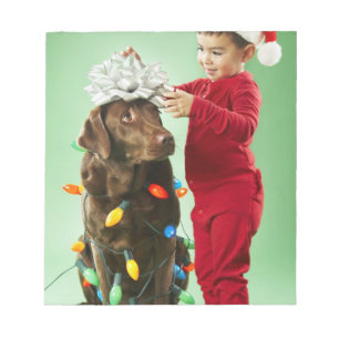 Young boy wrapping Christmas lights around a dog Notepad