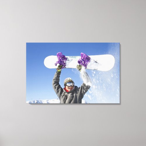 Young man holding his snowboard above his head canvas print