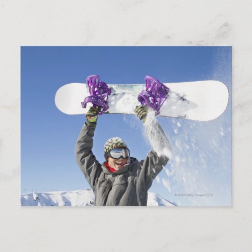 Young man holding his snowboard above his head postcard