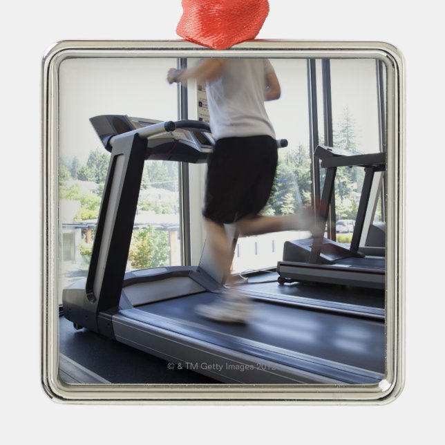 Young man running on a treadmill at health club, metal ornament (Front)