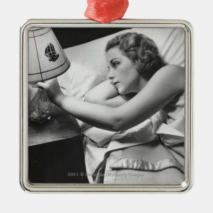 Young woman lying on bed turning off lamp on metal ornament