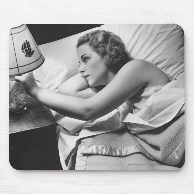 Young woman lying on bed turning off lamp on mouse pad (Front)