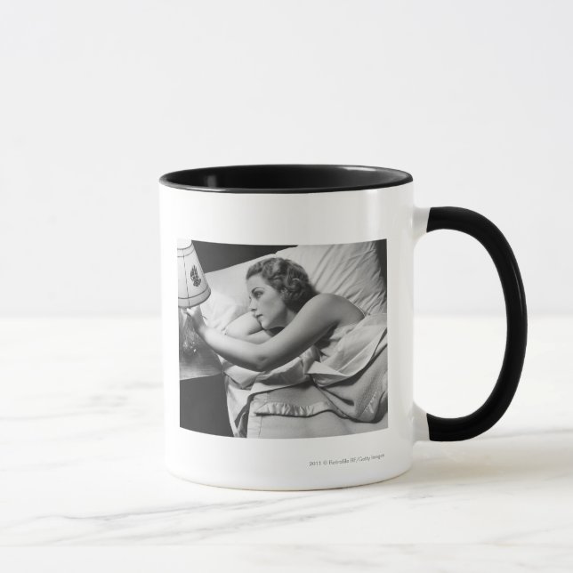 Young woman lying on bed turning off lamp on mug (Right)